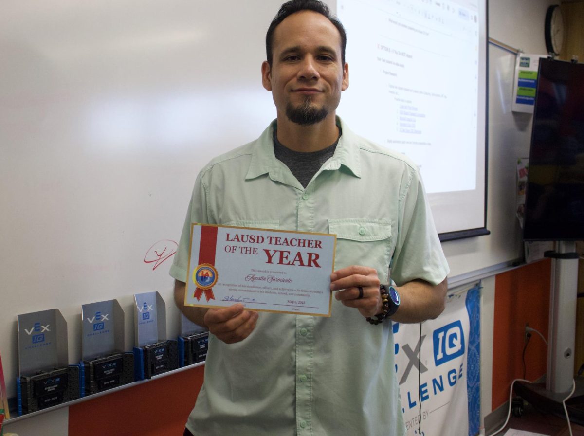 FROM CODE TO KUDOS - Mr. Sarmiento holds up a certificate of recognition presented by the school next to his various VEX Robotics Competition trophies for receiving the award of Teacher of the Year.