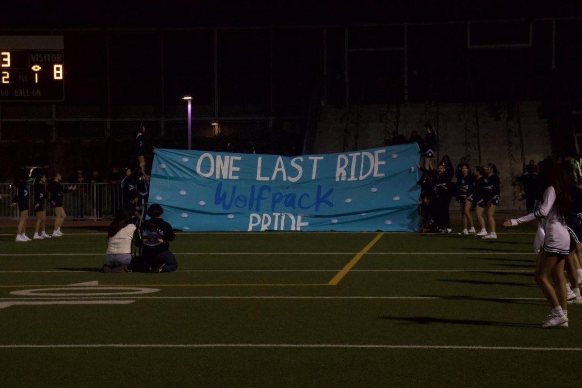 Cheerleaders hold up a “One Last Ride” banner as the Wolfpack prepares to take the field for Senior Night, celebrating the team’s final home game of the season.